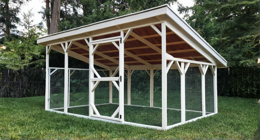 Wooden chicken coop with a roof in a grassy area with trees in the background