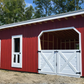 Red and white wooden shed with horse stall design in a natural setting