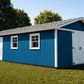 Blue storage shed with white doors on a grassy area with trees in the background
