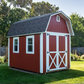 Red barn-style shed with white trim in a garden setting
