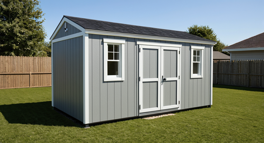 Gray storage shed with white trim on a grassy area with trees and a clear sky.